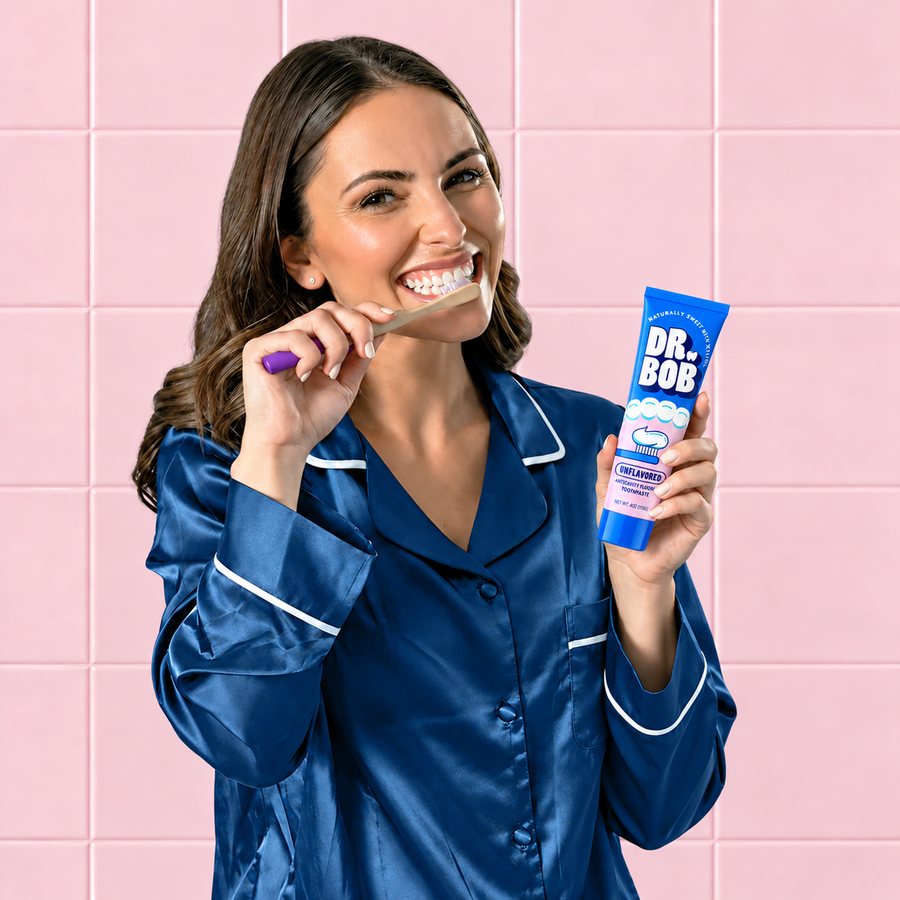 A smiling woman brushing her teeth and holding a tube of Dr. Bob